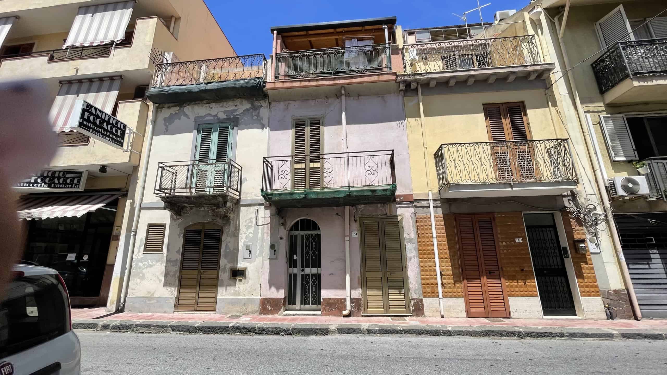 Edificio residenziale in Via Roma 168 a Scaletta Zanclea, con balconi e facciata in condizioni di usura, situato nel centro del paese.