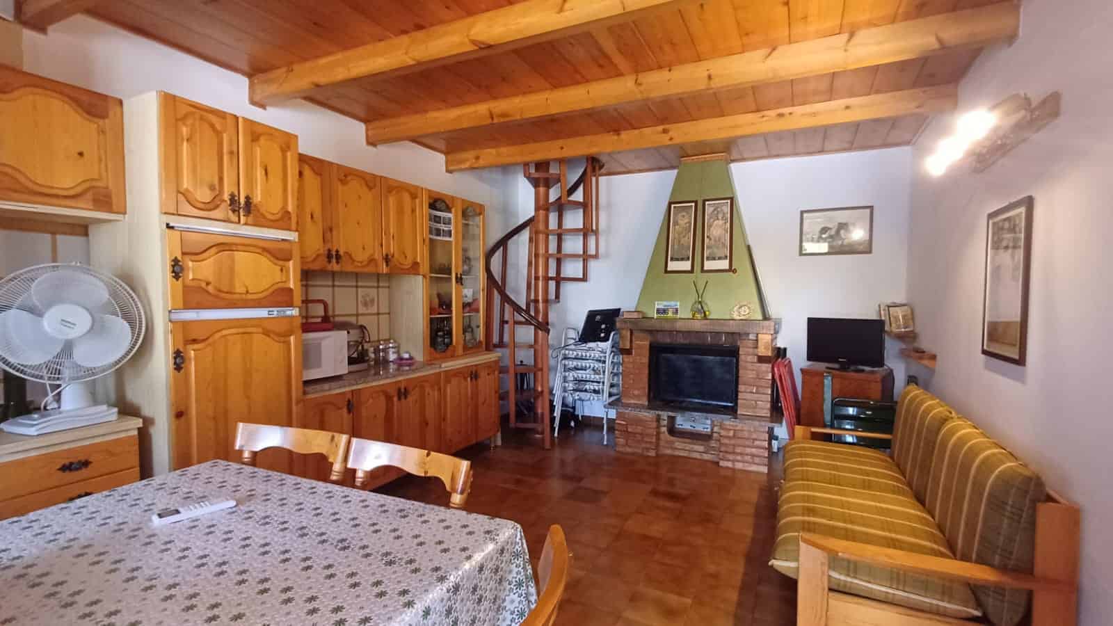 Interno di una villetta con cucina e zona soggiorno, soffitto in legno e camino in pietra, arredamento accogliente e rustico.