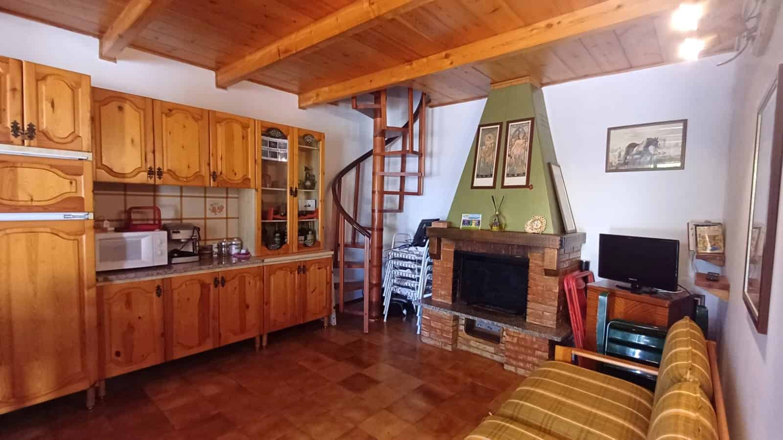 Interno di una villetta in affitto con cucina in legno, camino e zona soggiorno con divano e TV, ambiente caldo e accogliente.