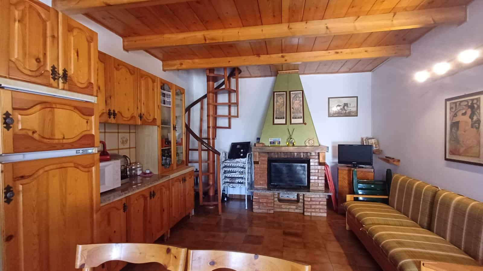 Interno di una casa con cucina in legno, camino e zona soggiorno con divano a righe, ambiente caldo e accogliente.
