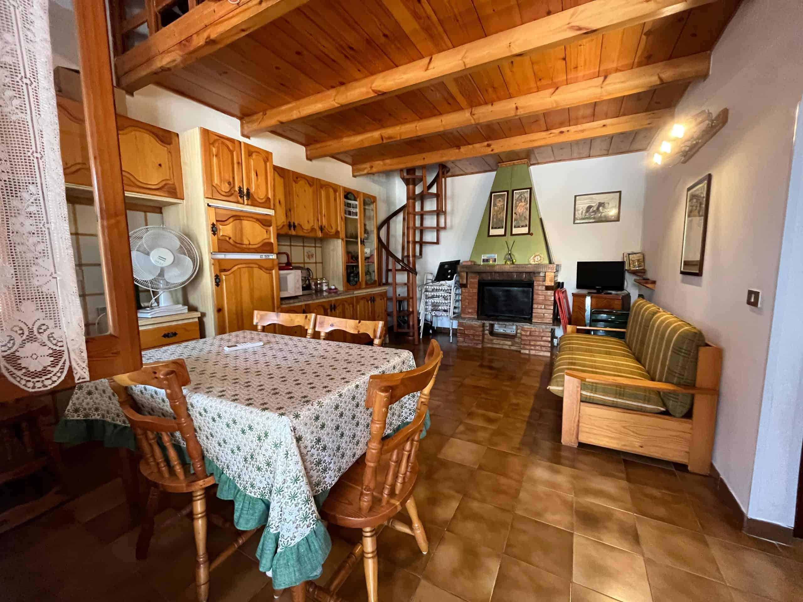 Interno di una villetta con zona soggiorno e cucina in stile rustico, soffitto in legno e pareti bianche.