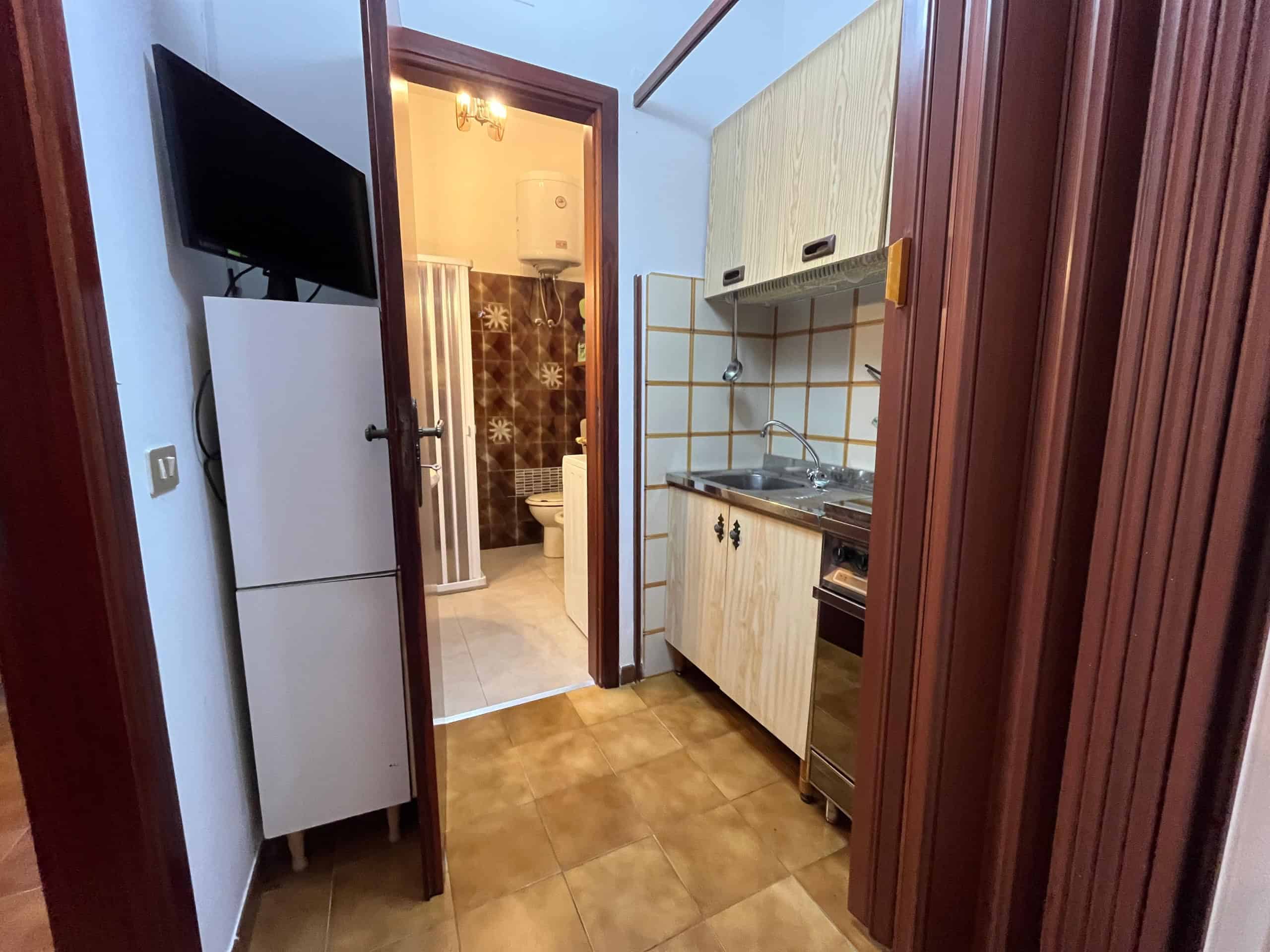 Interno di una villetta in affitto con cucina compatta e accessori, vista sulla porta del bagno.