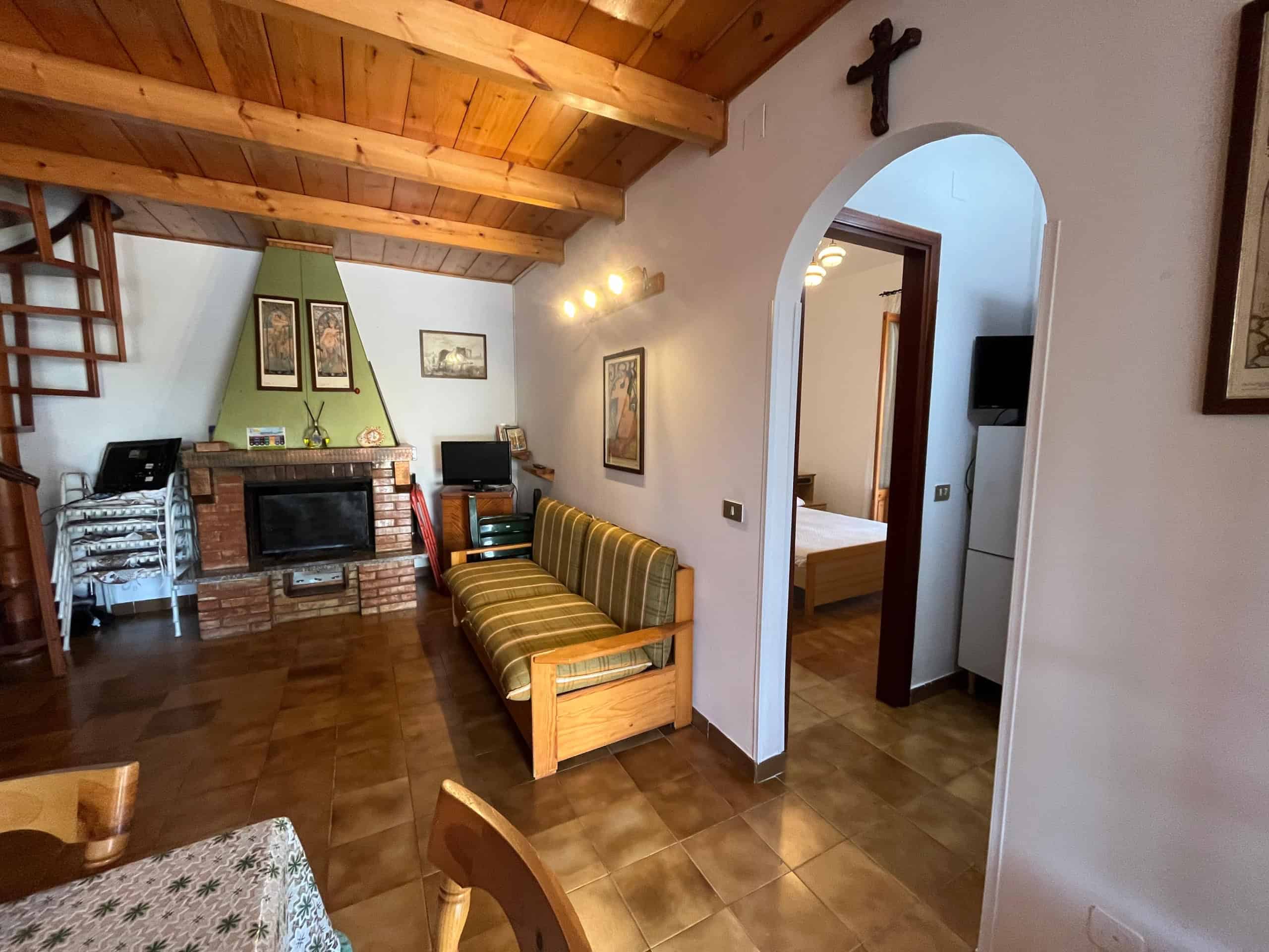 Interno di una villetta in affitto con soffitto in legno e zona soggiorno con camino e divani.