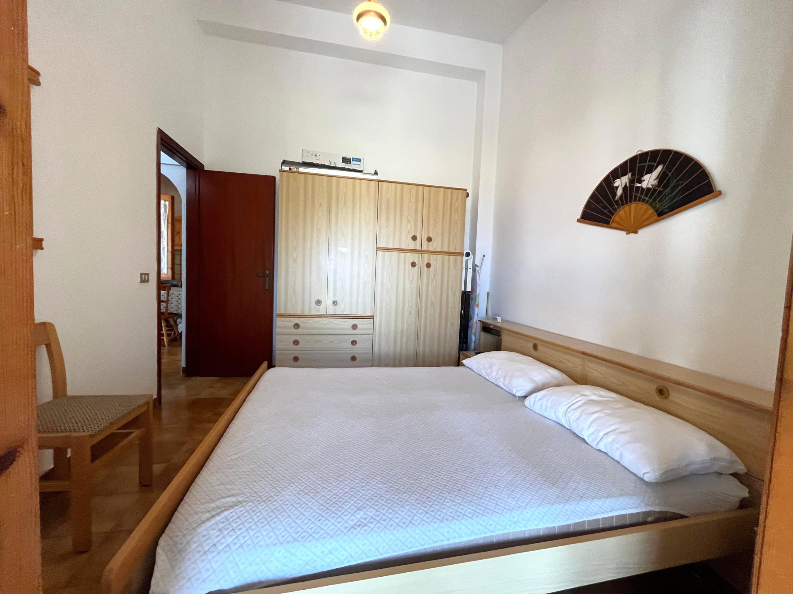 Camera da letto con letto matrimoniale, armadio in legno e decorazione a ventaglio sulla parete.