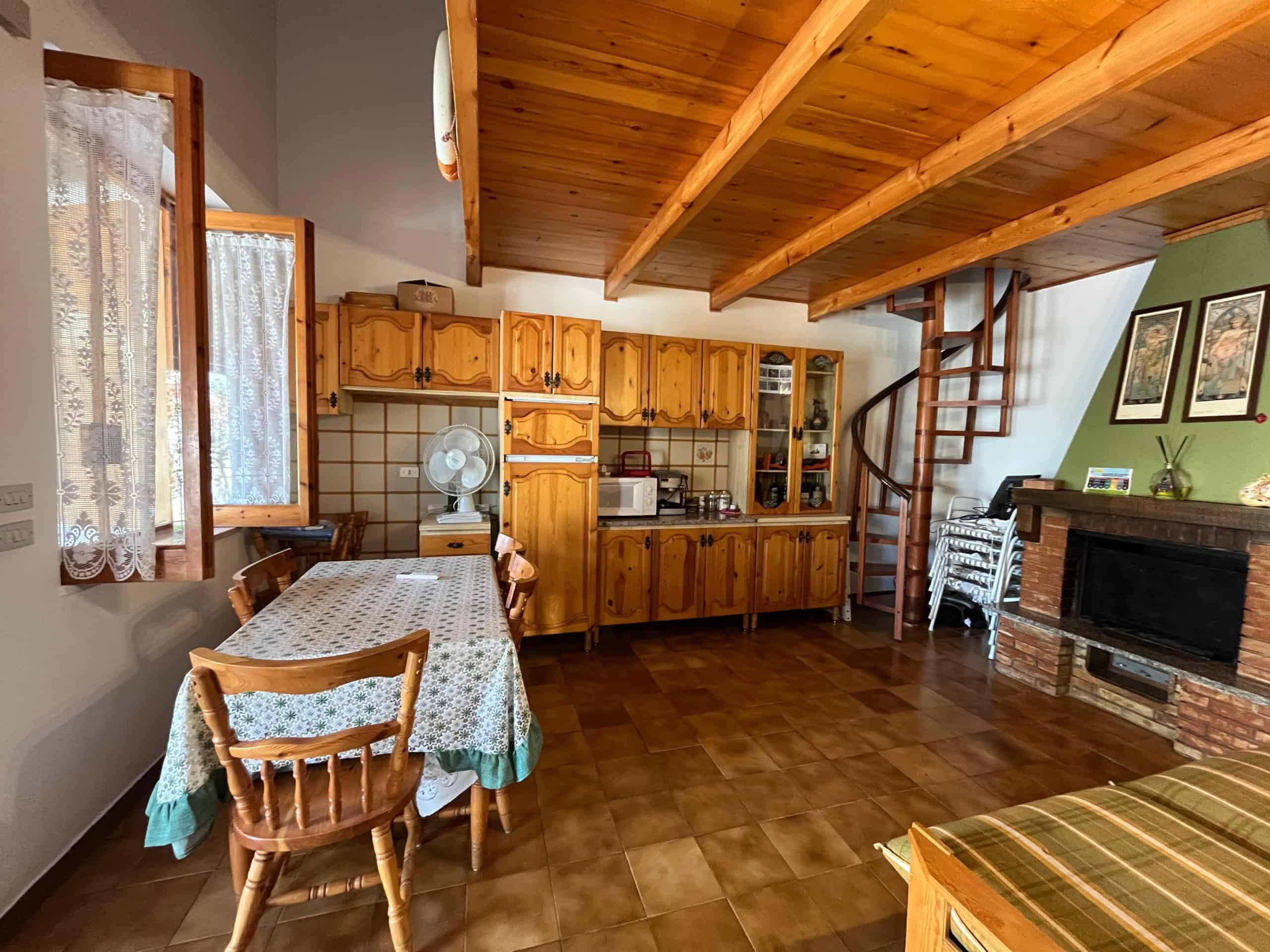 Interno di una villetta in affitto con cucina in stile rustico e zona soggiorno con camino, ambiente accogliente e luminoso.