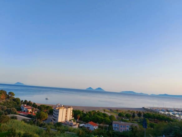 Vista panoramica del mare con isole sullo sfondo, case e vegetazione in primo piano, cielo sereno, rappresentando un paesaggio costiero tranquillo e suggestivo.