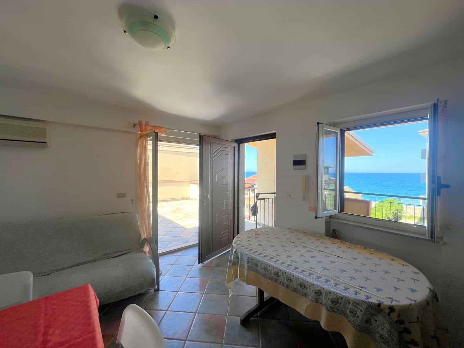 Ampia vista mare dalla finestra di una stanza luminosa con balcone, arredi semplici e atmosfera accogliente, ideale per soggiorni rilassanti vicino alla spiaggia.