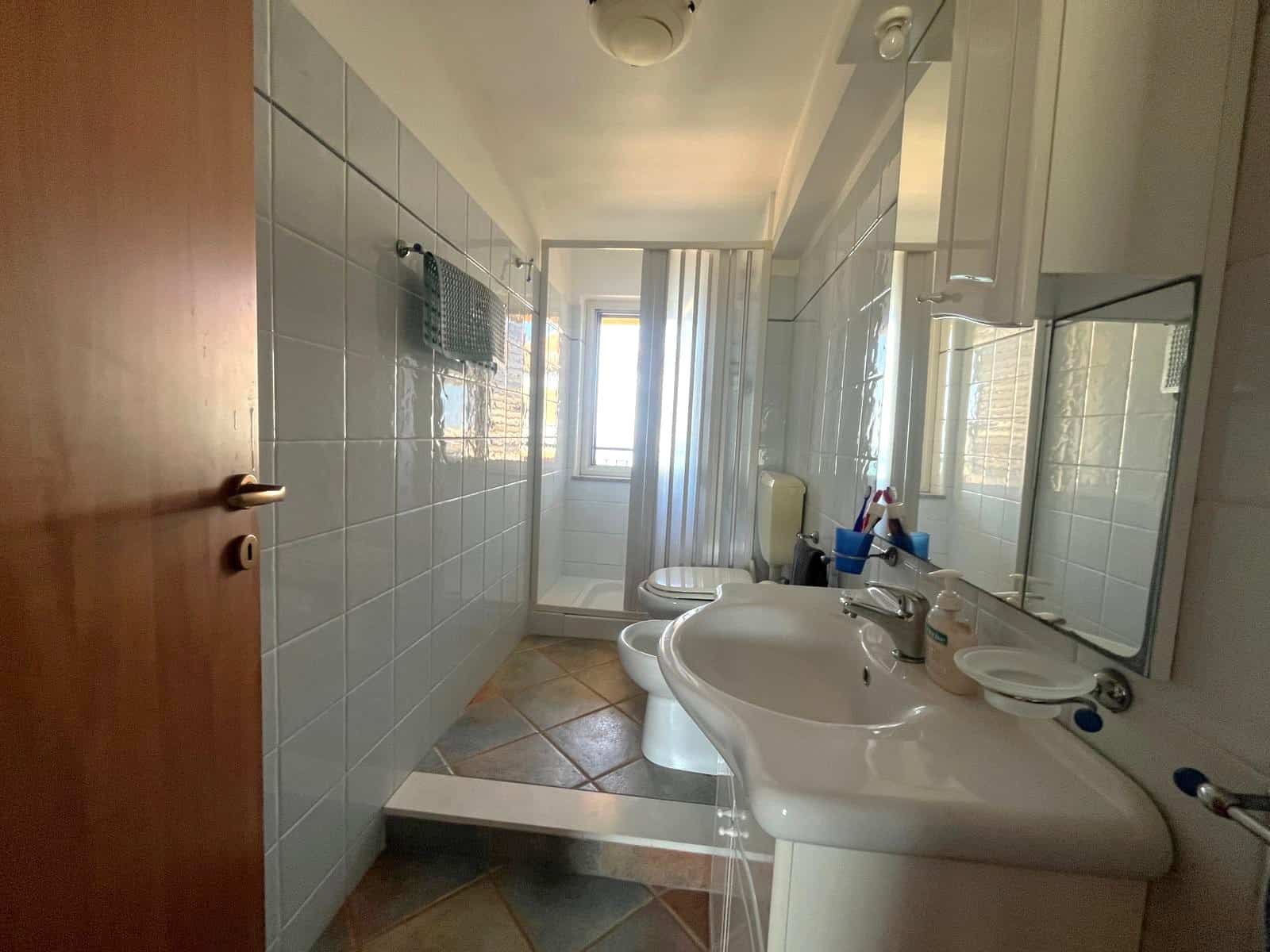 Il bagno luminoso con lavabo, specchio e finestra, arredato in stile semplice e funzionale, ideale per una casa o un appartamento in vendita o affitto.
