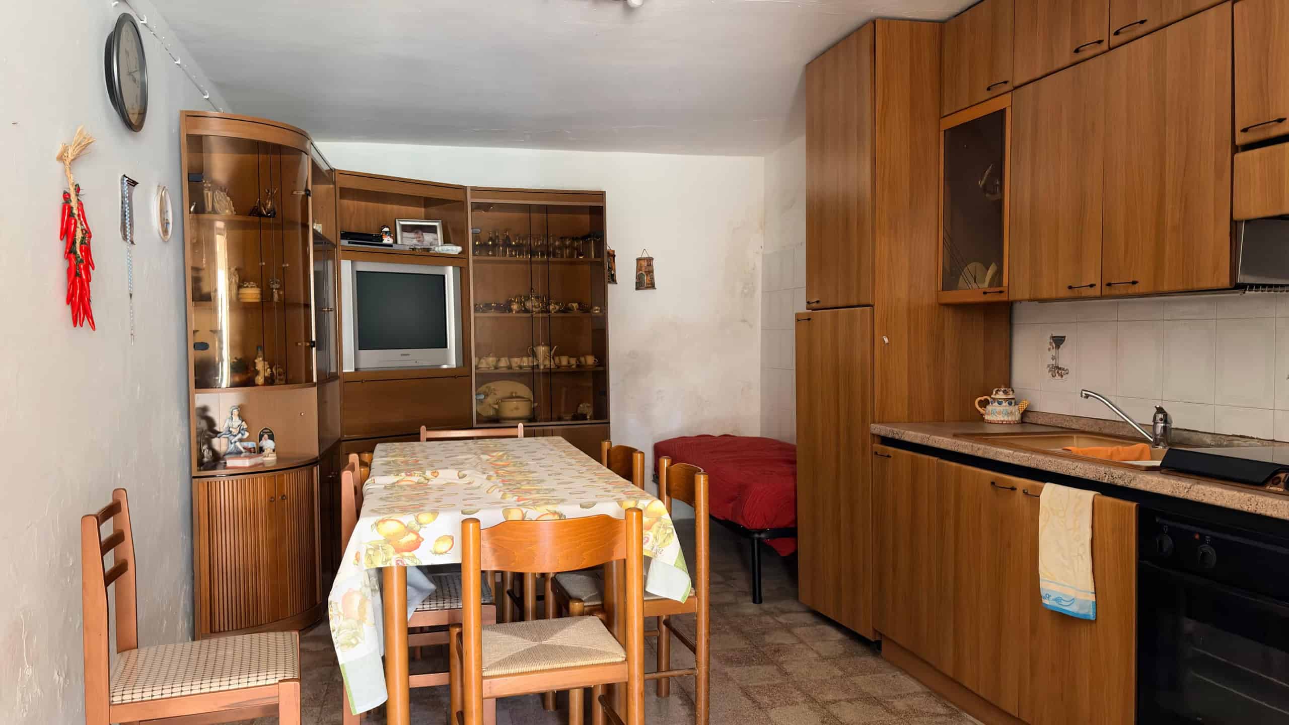 Ampia cucina abitabile con mobili in legno, tavolo da pranzo, televisore e armadietti, ambiente accogliente e funzionale, ideale per vivere momenti conviviali e preparare pasti in famiglia.