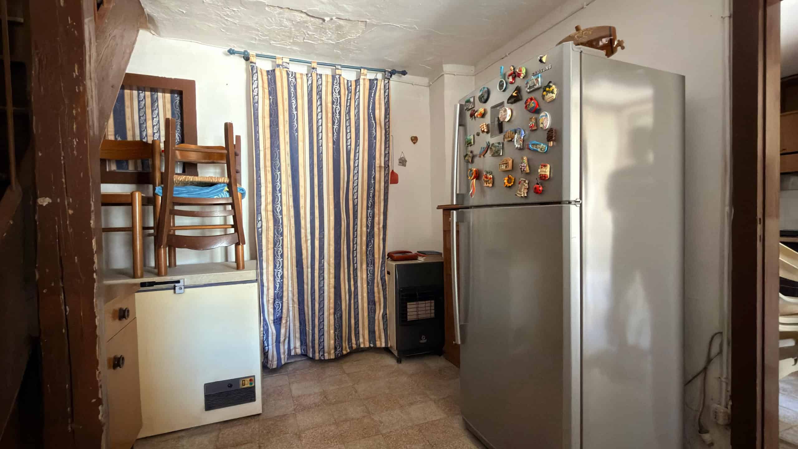 Ampio frigorifero in cucina con decorazioni colorate sulla porta, vicino a un termosifone e a un mobile in legno, in un ambiente domestico luminoso e accogliente.