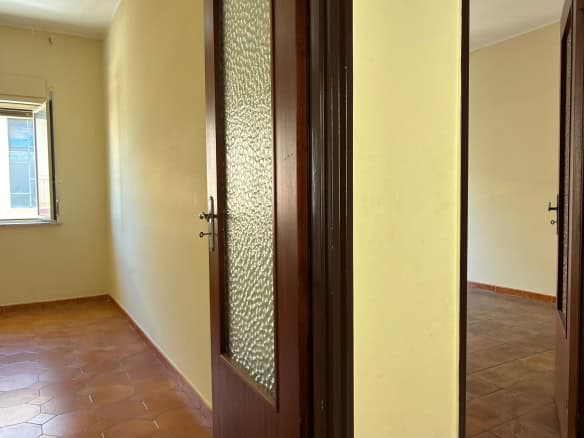 Ampia stanza luminosa con pareti beige, pavimento in piastrelle e finestra che permette l'ingresso di luce naturale, ideale per ambienti residenziali.