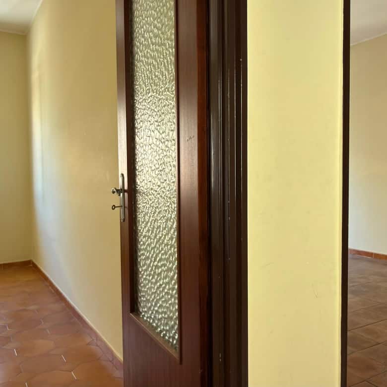Ampia stanza luminosa con pareti beige, pavimento in piastrelle e finestra che permette l'ingresso di luce naturale, ideale per ambienti residenziali.