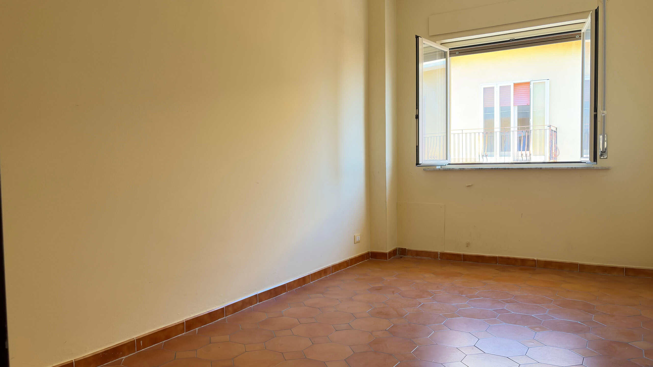 Spazio vuoto in una stanza luminosa con pareti beige e pavimento in piastrelle di terracotta, pronta per essere arredato o ristrutturato.