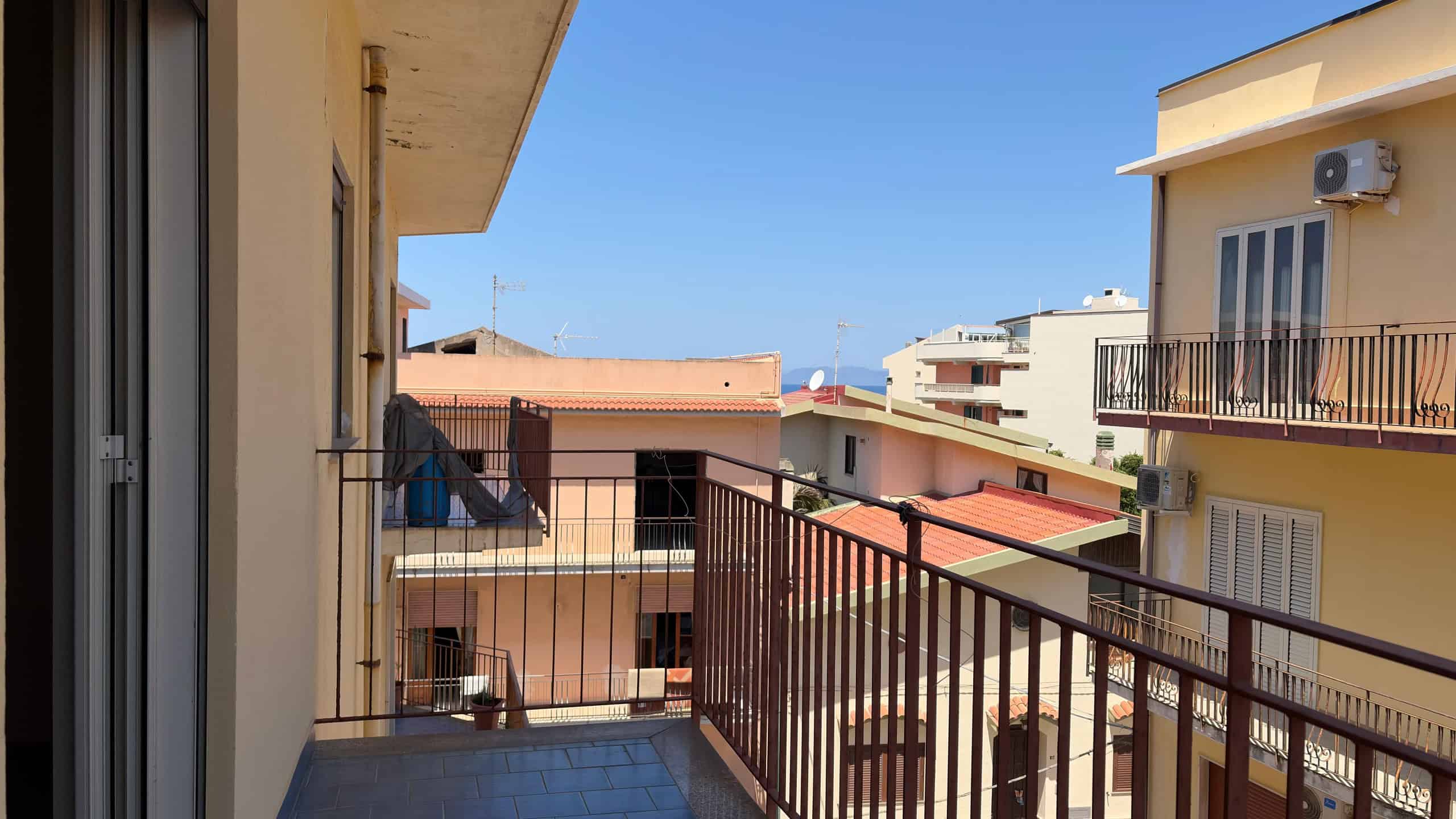 Ampio balcone con vista su edifici residenziali e cielo azzurro, ideale per relax e momenti all'aperto in città.