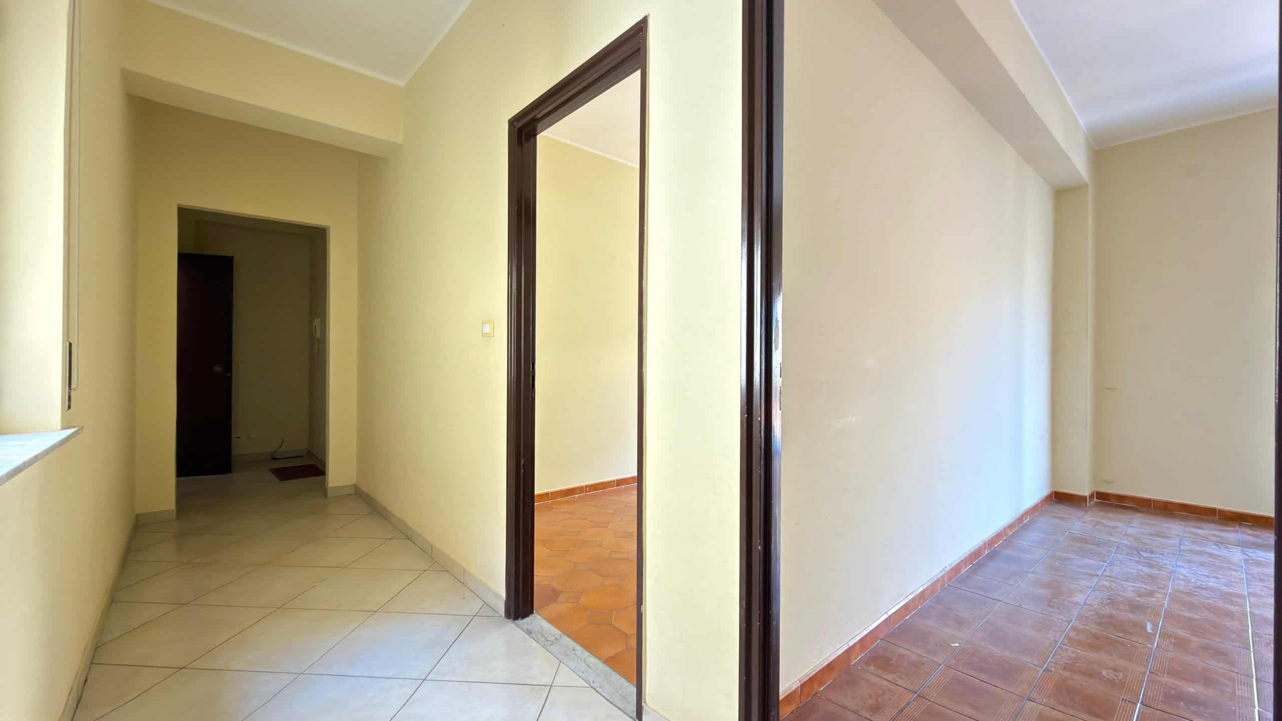 Ampia vista di un interno residenziale con pareti beige, pavimenti in ceramica e ingresso a due stanze separate, ideale per appartamenti moderni e luminosi.