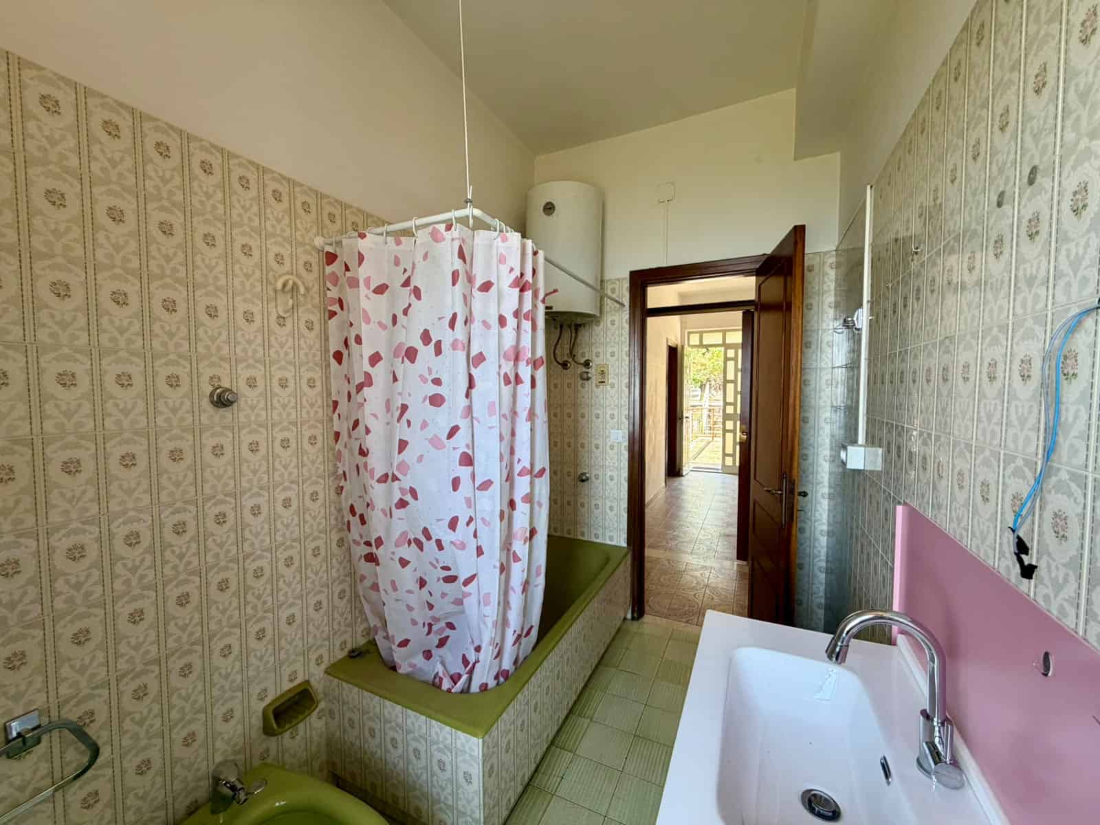 Doccia e vasca da bagno in un bagno spazioso con pareti rivestite di piastrelle vintage, lavabo moderno e accesso a un corridoio luminoso, ideale per case in vendita o affitto a NextCasa.