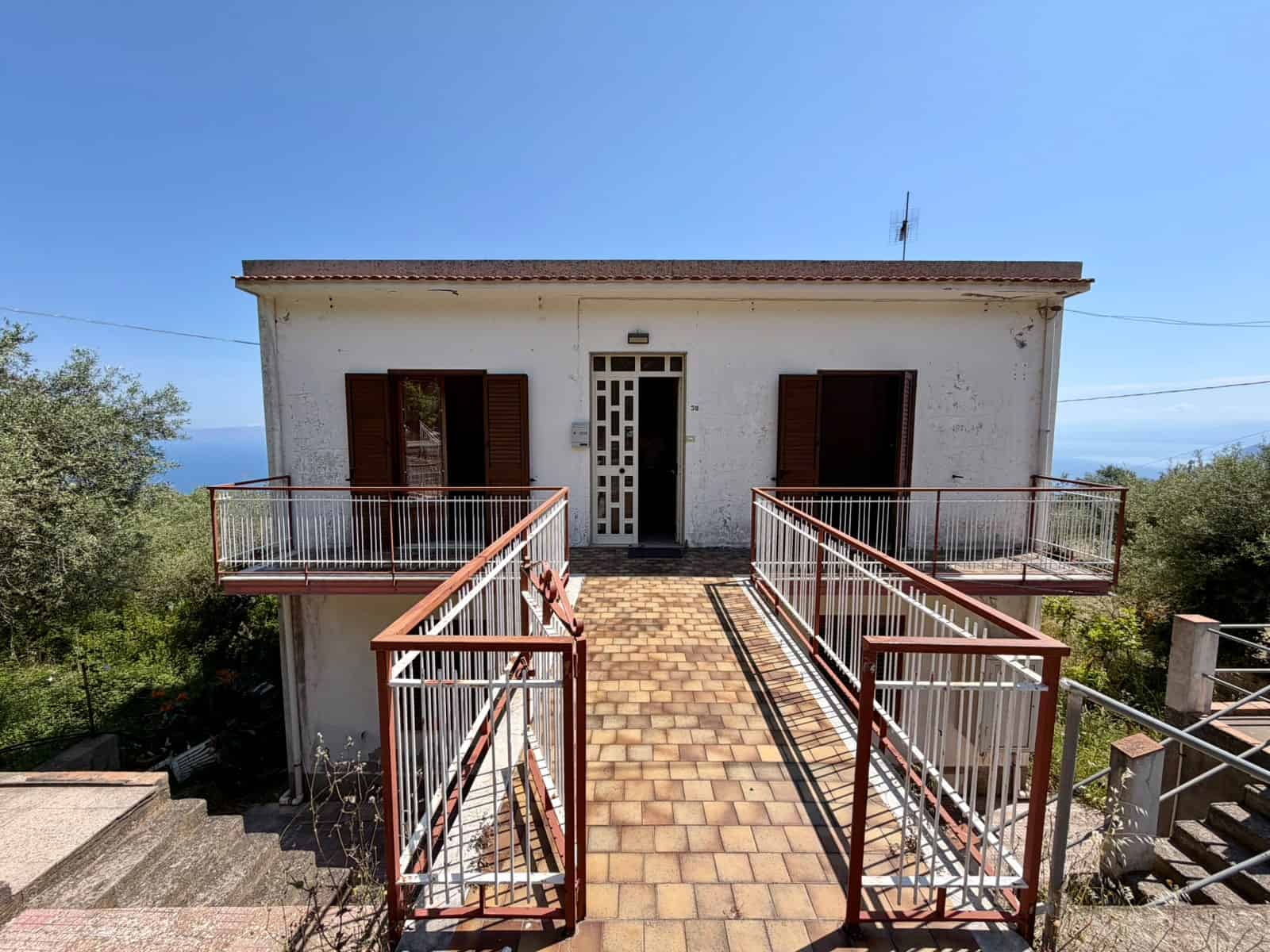 Escalatore esterno con vista panoramica sul mare, accessibile tramite passerella in ferro battuto, in una casa di campagna in stile rustico, immersa nella natura e con un cielo azzurro limpido.