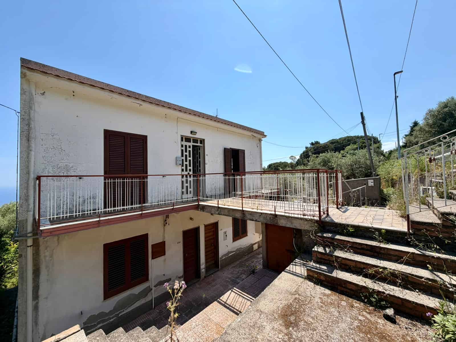Una casa indipendente con balcone e scale esterne, immersa in un ambiente naturale, ideale per residenze in campagna o case di vacanza in Italia.