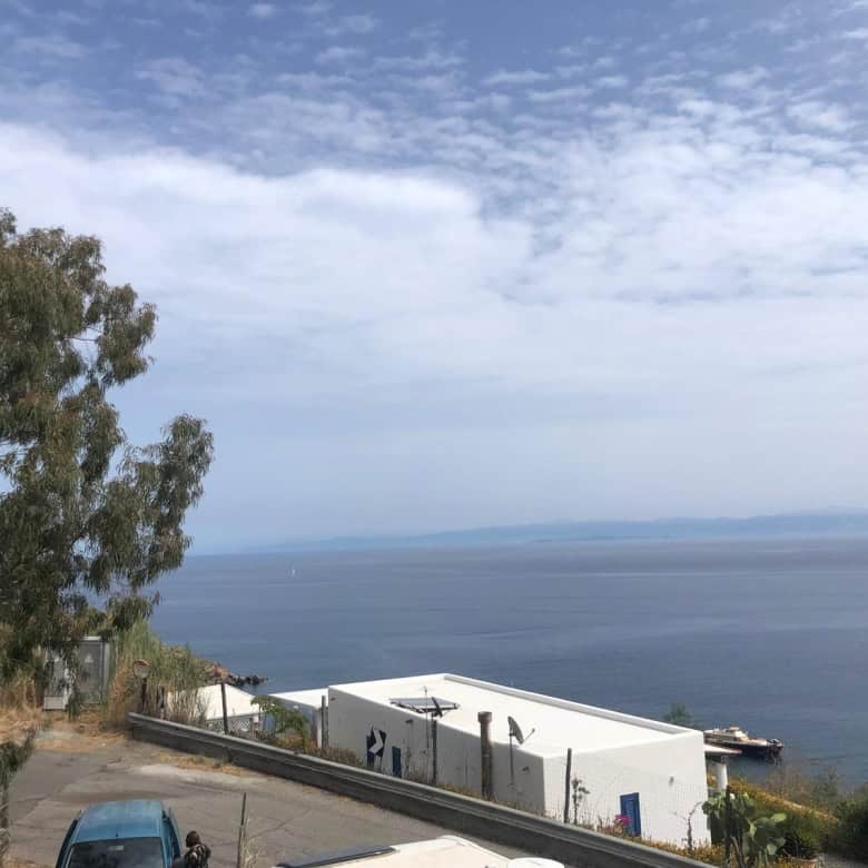 VISTA PANORAMICA DEL MARE E DELLA COSTA CON EDIFICI BIANCHI E STRADA, PAESAGGIO COSTIERO IN ITALIA, CIELO PARZIALMENTE NUVOLOSO, ATMOSFERA SERENA E RILASSANTE.