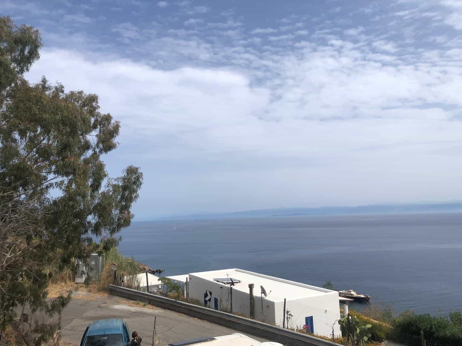 VISTA PANORAMICA DEL MARE E DELLA COSTA CON EDIFICI BIANCHI E STRADA, PAESAGGIO COSTIERO IN ITALIA, CIELO PARZIALMENTE NUVOLOSO, ATMOSFERA SERENA E RILASSANTE.