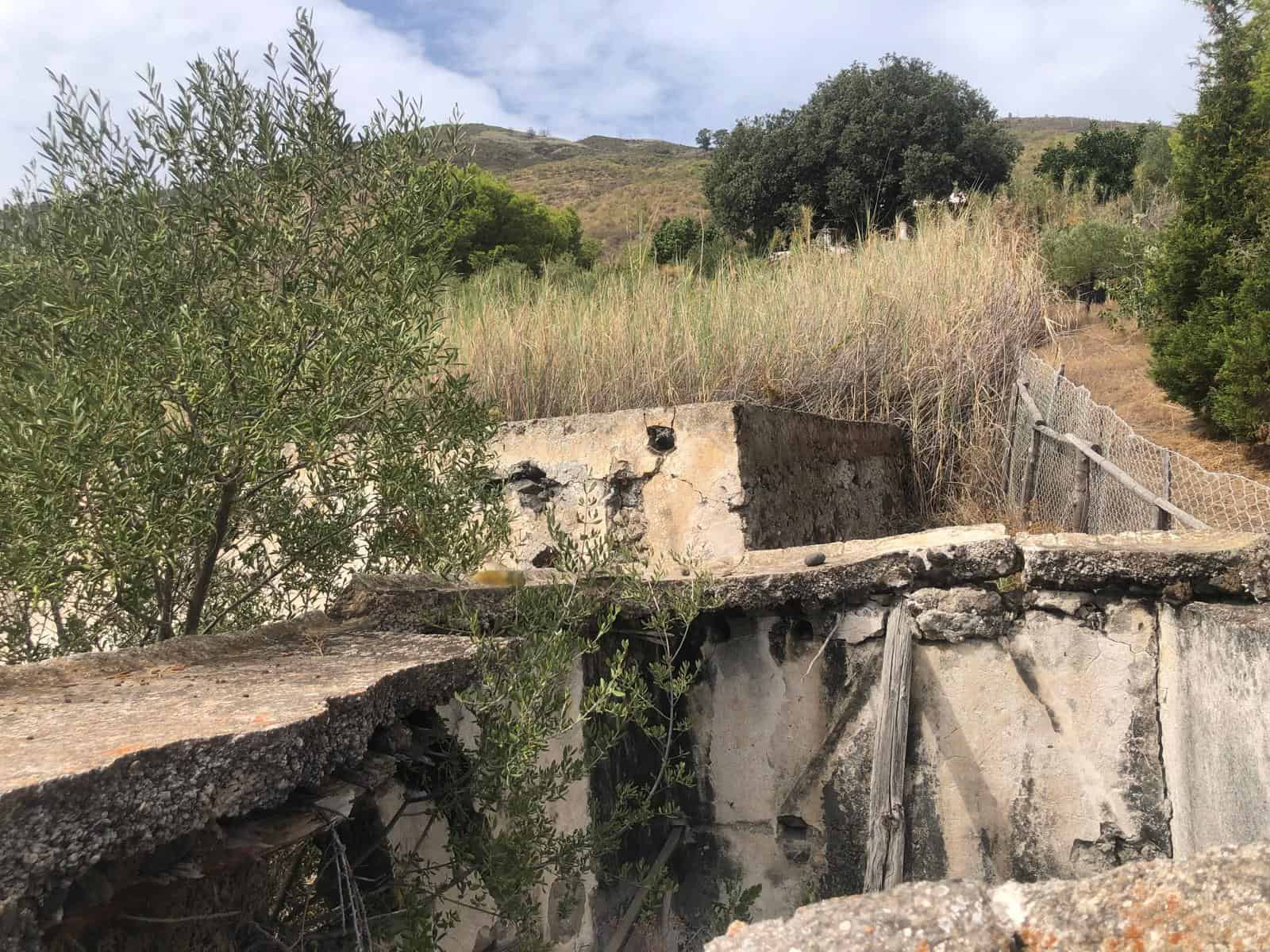 Resti di un edificio abbandonato in campagna con muri in pietra e vegetazione circostante, scenario rurale e storico.