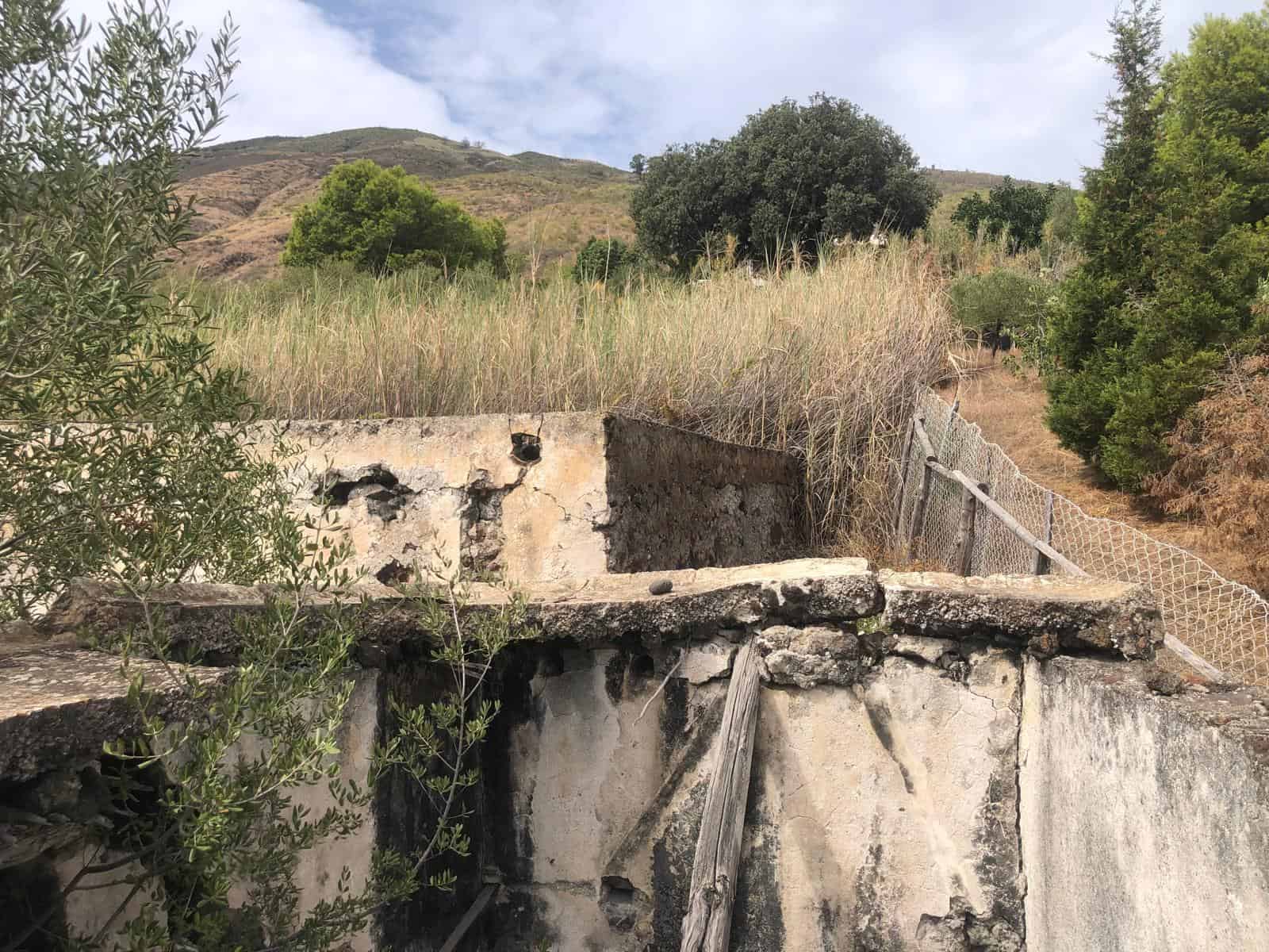 Pannello di cemento abbandonato in un'area naturale con vegetazione e colline sullo sfondo, rappresenta un elemento di decadenza e natura incontaminata.