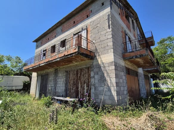 Abitazione in costruzione con struttura in cemento e balconi in ferro, immersa nel verde e in un ambiente naturale, pronta per essere completata e personalizzata.