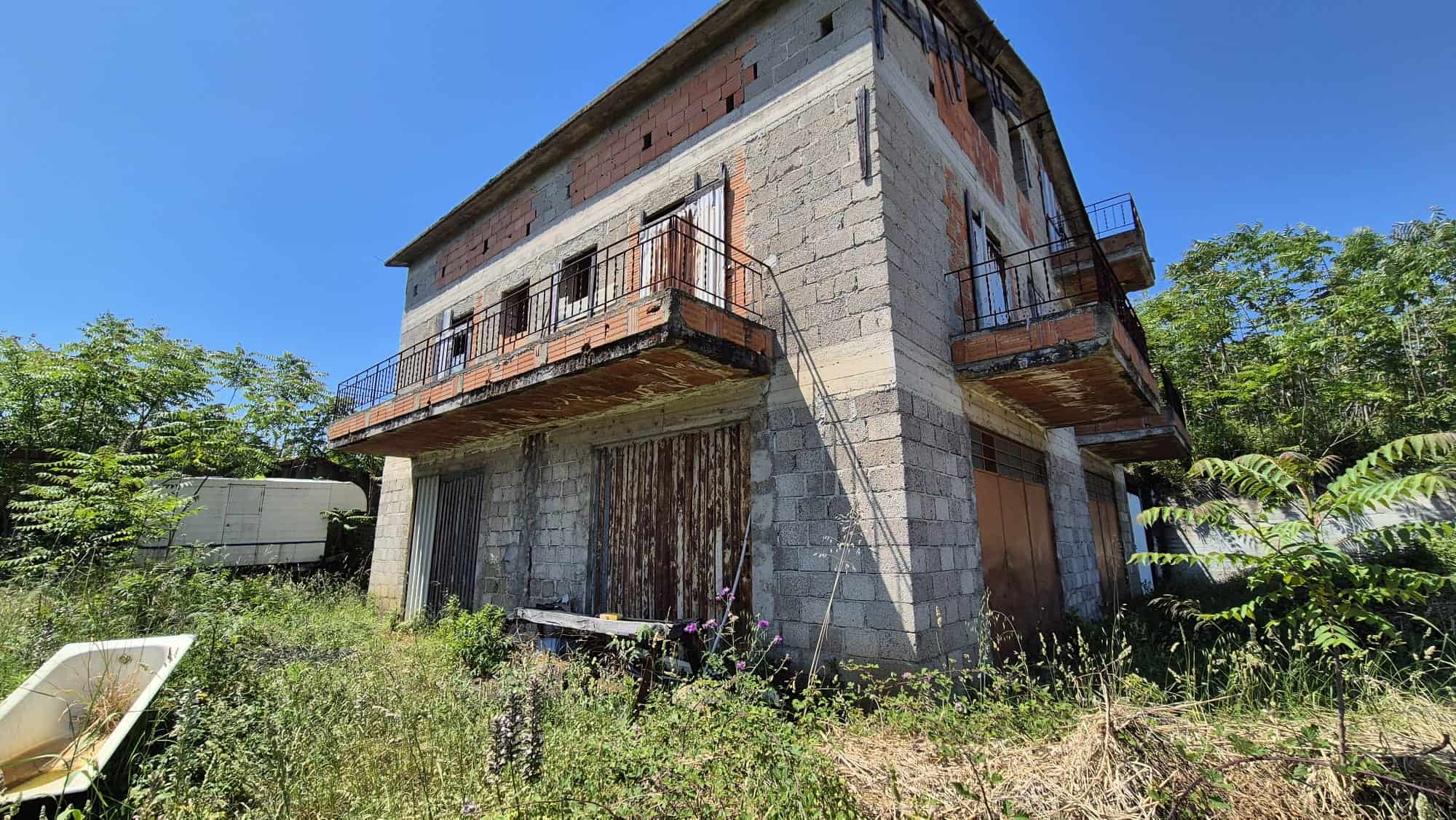 Abitazione in costruzione con struttura in cemento e balconi in ferro, immersa nel verde e in un ambiente naturale, pronta per essere completata e personalizzata.