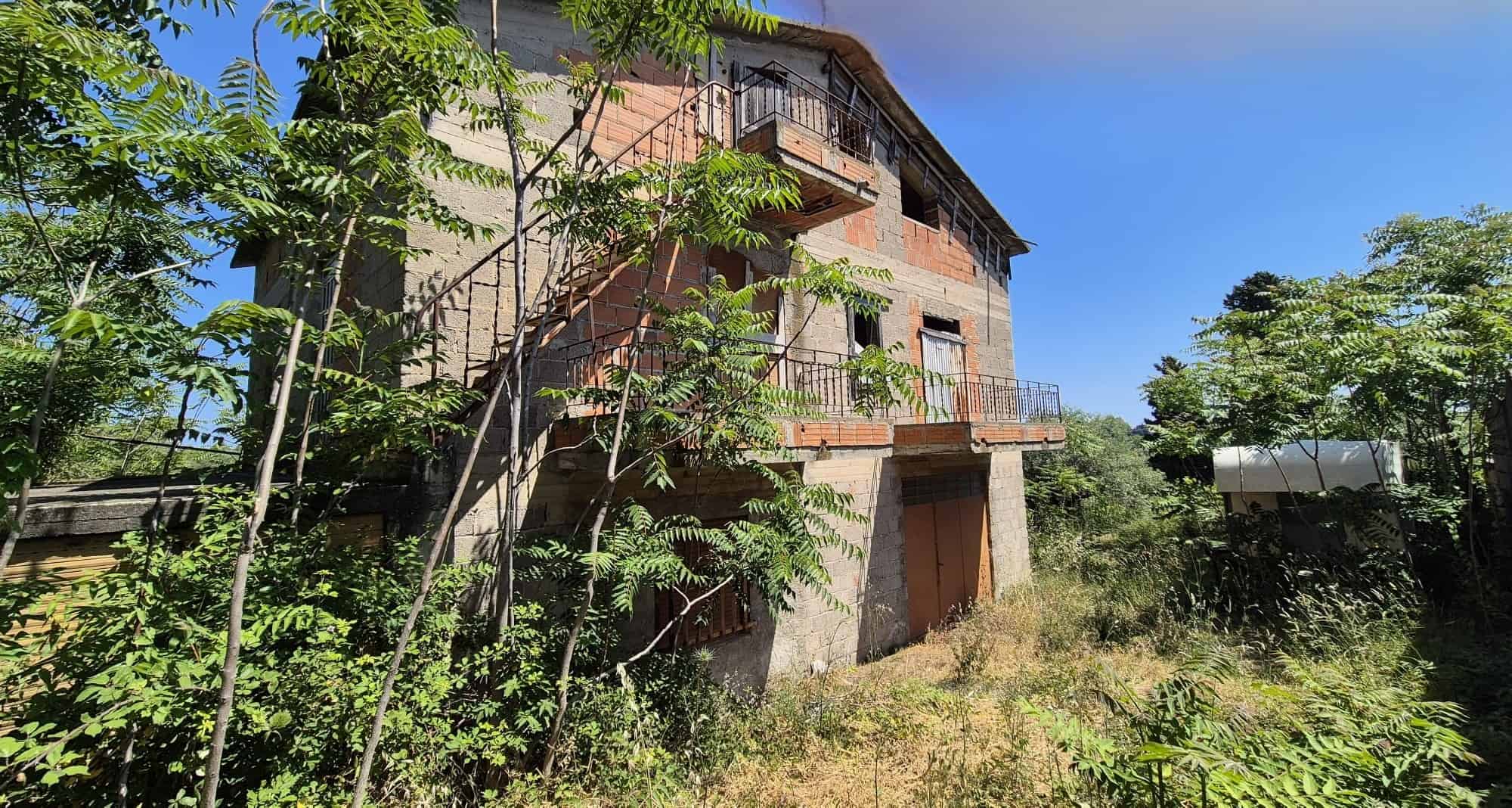 Vecchio edificio residenziale in mattoni con balconi e terrazza, immerso nel verde e circondato da alberi, in un contesto rurale e tranquillo.