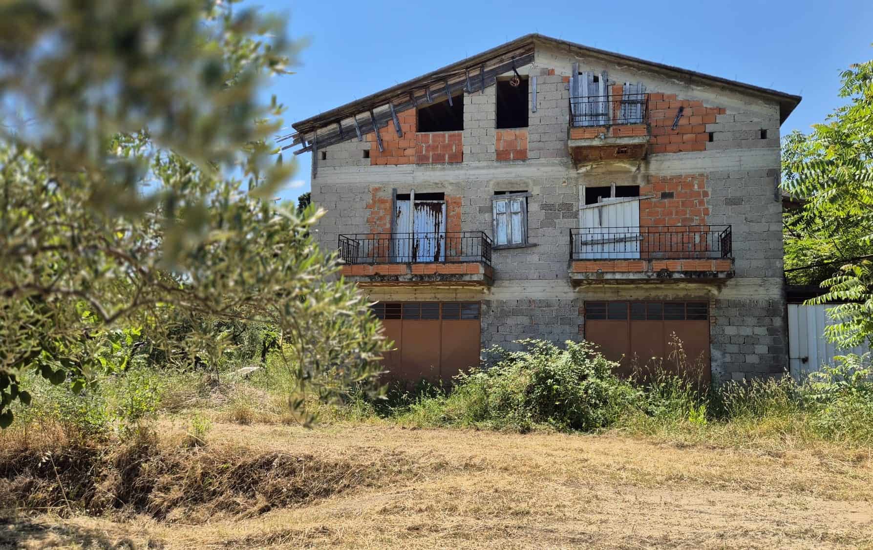 Vecchio edificio residenziale in fase di ristrutturazione con balconi e finestre, immerso nel verde, pronto per essere trasformato in una casa moderna e confortevole.