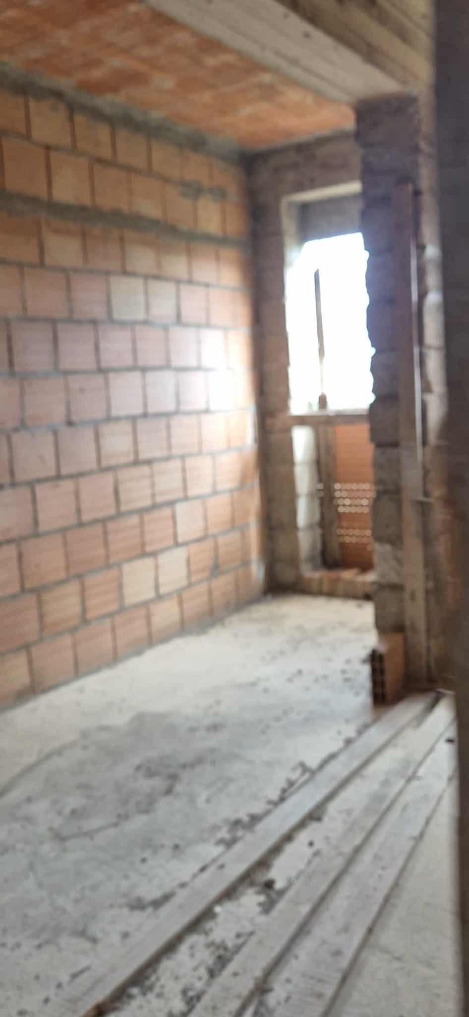 Ampio spazio interno in fase di costruzione con pareti in mattoni e finestra che permette l'ingresso di luce naturale, pronto per essere rifinito e personalizzato.