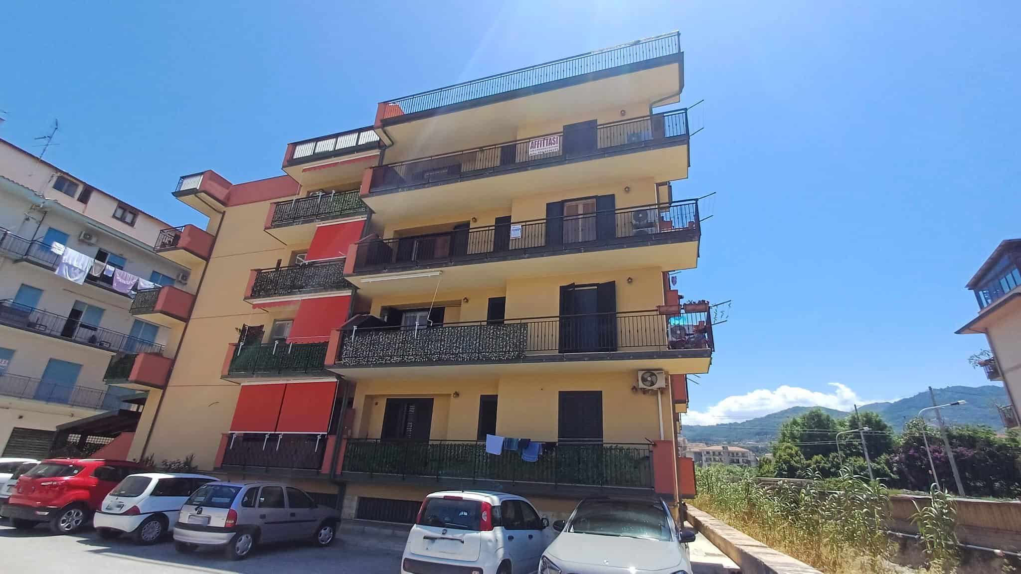 Ampio edificio residenziale con balconi e facciata colorata, situato in un'area urbana con veicoli parcheggiati e paesaggi montani sullo sfondo, ideale per investimenti immobiliari in Italia.