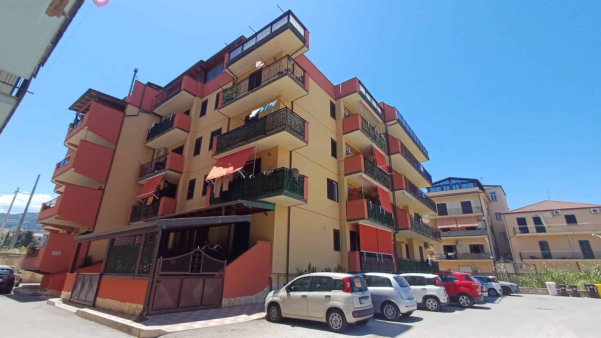 Balcone di un edificio residenziale moderno con facciata colorata, parcheggio sottostante e vista urbana, rappresentativo di immobili in vendita o affitto a NextCasa.