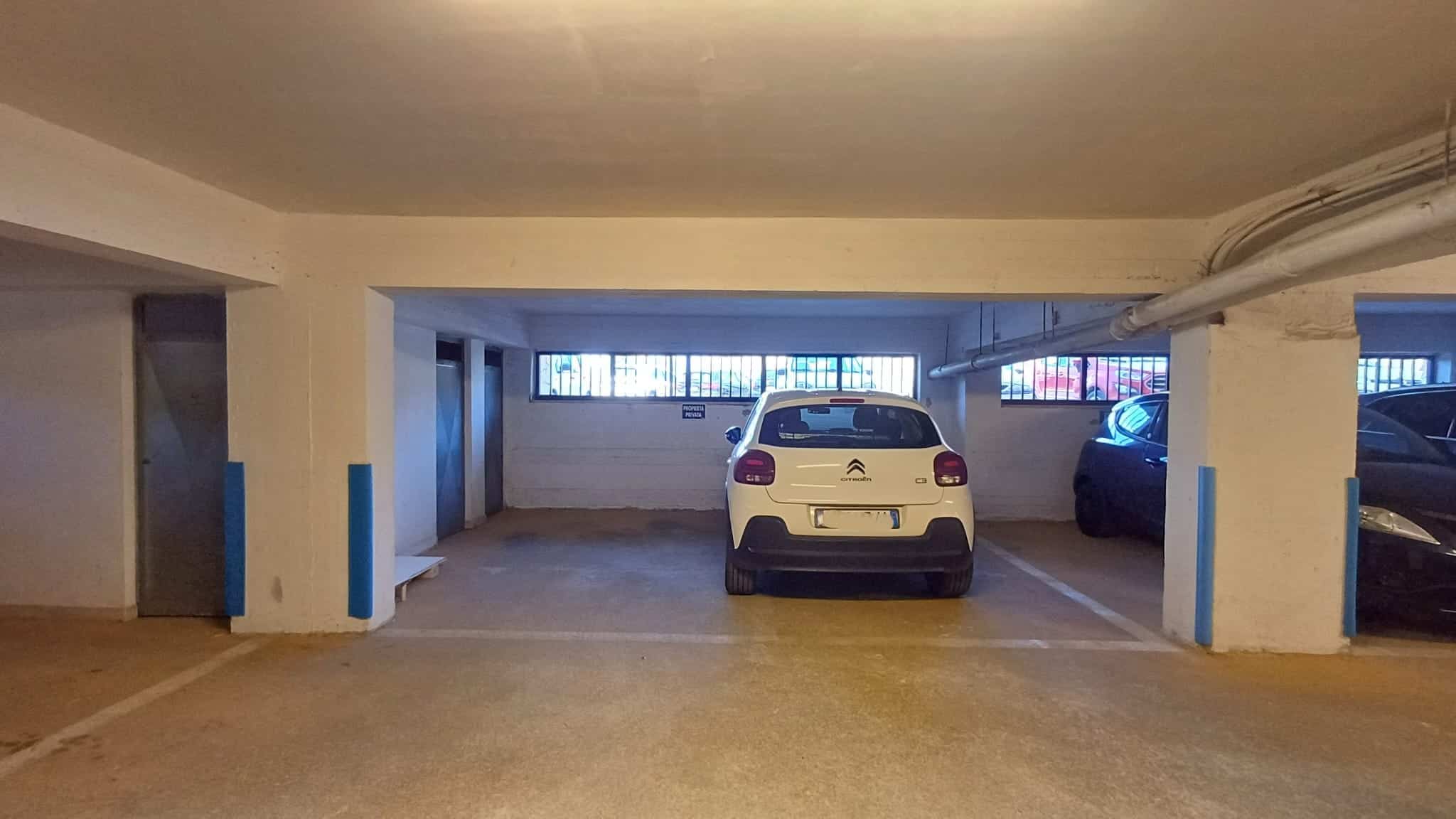 Auto compatta parcheggiata in un garage sotterraneo, con pareti bianche e colonne blu, illuminato da luci artificiali, con altri veicoli parcheggiati nelle vicinanze.