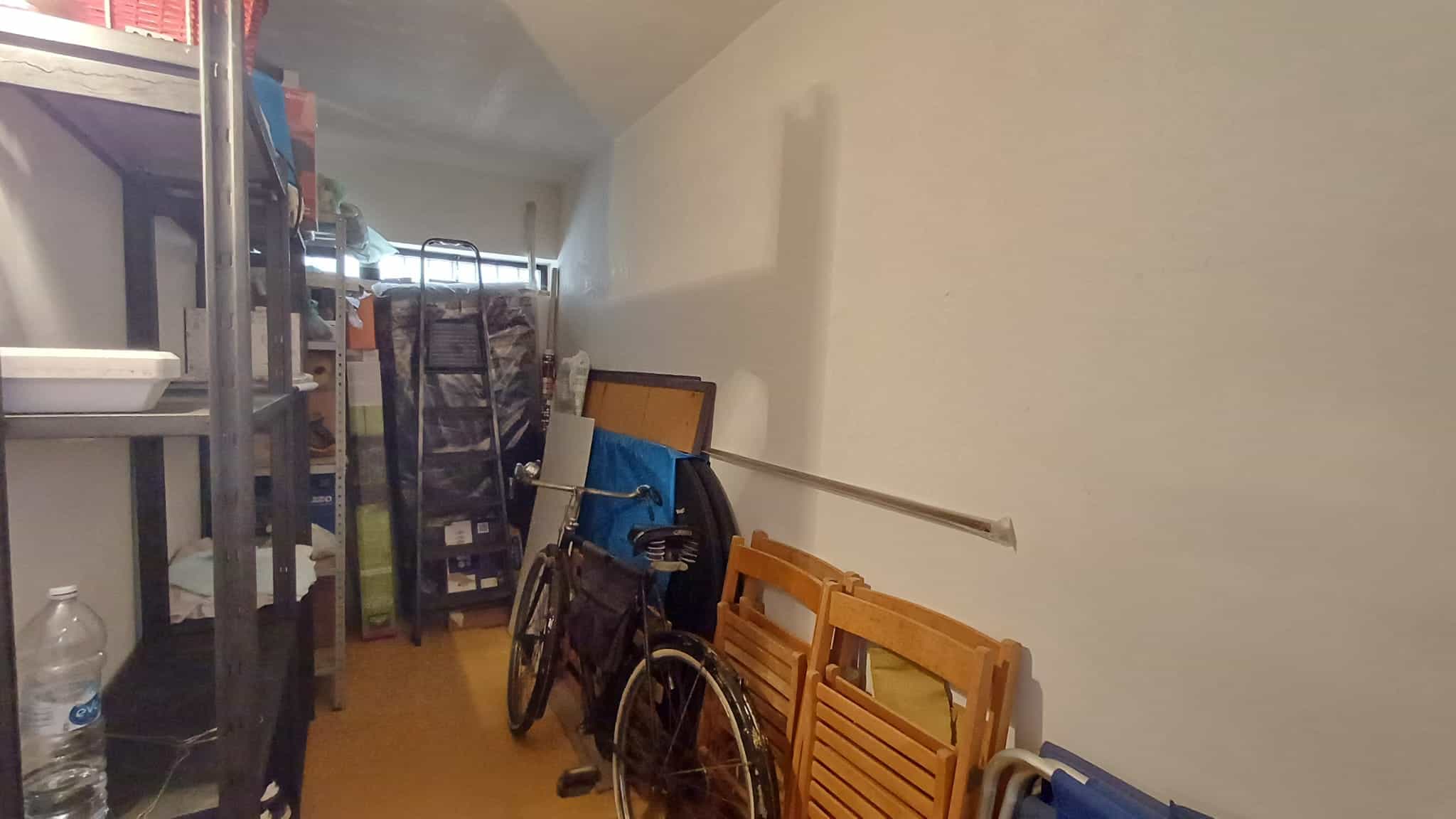 Sedie pieghevoli e biciclette in un magazzino o ripostiglio, con scaffali e oggetti vari, ambiente ordinato e funzionale per lo stoccaggio domestico.