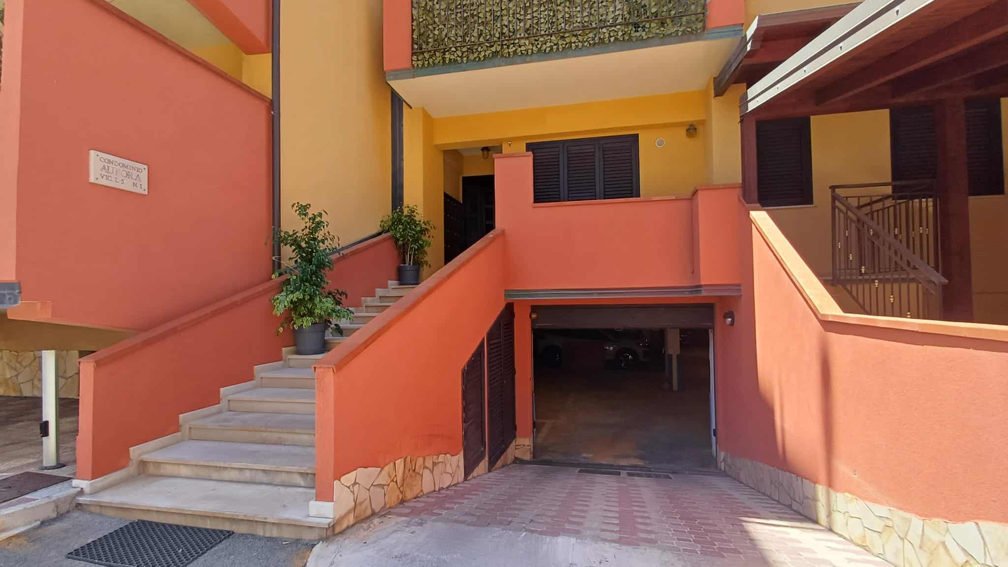 Ampio garage sotterraneo con accesso tramite rampa e scale, situato in un edificio residenziale colorato con pareti arancioni e dettagli in legno, ideale per parcheggio e deposito auto.