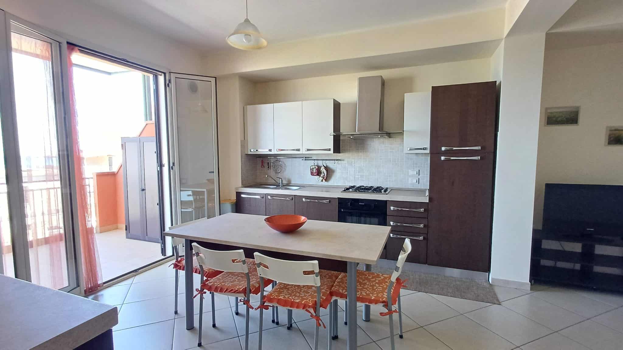 Spazio cucina moderno con mobili bianchi e marroni, area pranzo con tavolo e sedie, balcone con vista luminosa, ideale per vivere in comfort e stile.