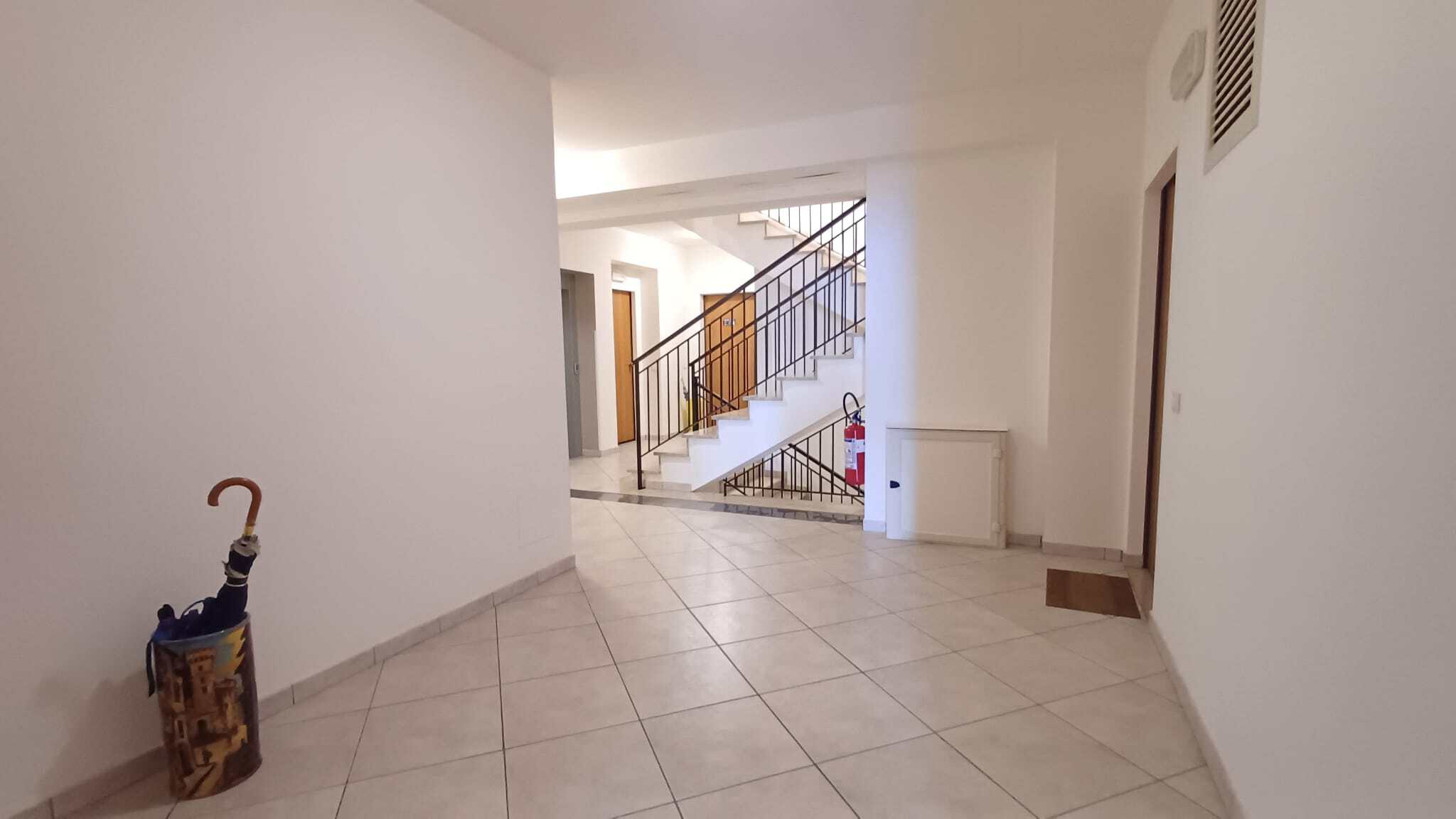 Ampio ingresso di un appartamento con pareti bianche, pavimento in piastrelle e scala interna in legno e ferro, ambiente luminoso e accogliente, ideale per residenze moderne e confortevoli.