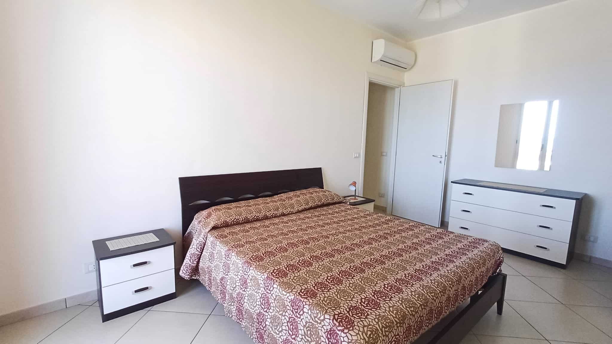 Ampia camera da letto moderna con letto matrimoniale, comodini e cassettiera, ambiente luminoso e arioso, ideale per residenze di comfort e stile. Perfetta per chi cerca eleganza e funzionalità.
