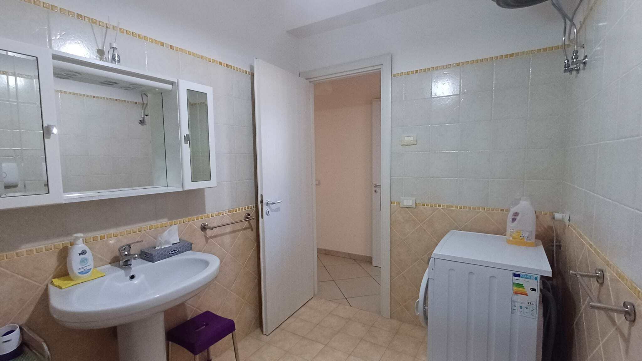 Lavatrice e lavabo in bagno con pareti rivestite di piastrelle bianche, spazio funzionale e ben illuminato, ideale per servizi domestici e lavanderia.