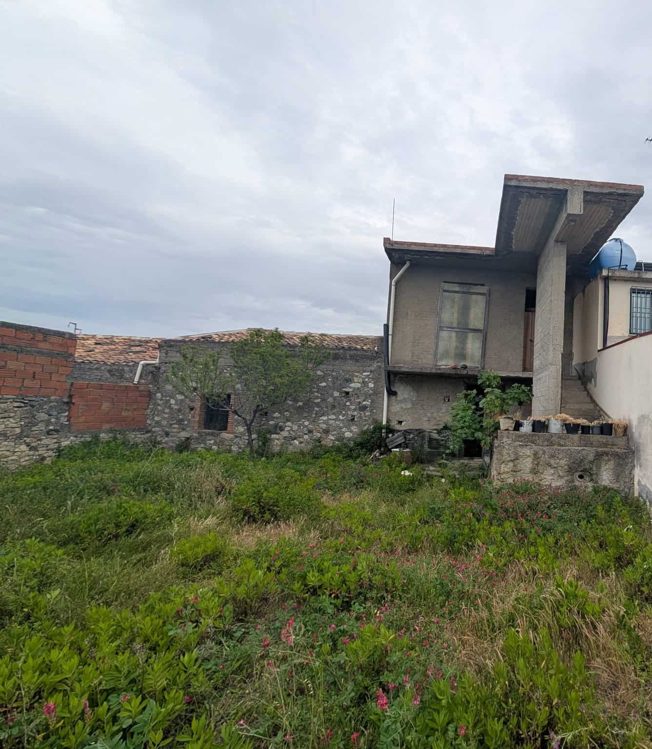 Balcone e facciata di una casa in costruzione o ristrutturazione con giardino verde e cielo nuvoloso, in un'area residenziale di prossima realizzazione.