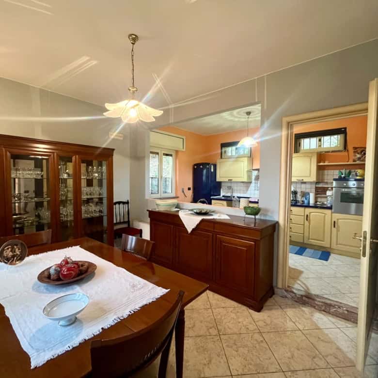 Elegante sala da pranzo con mobili in legno, vetrina con cristalli e tavolo decorato con frutta fresca, in un ambiente luminoso e accogliente.