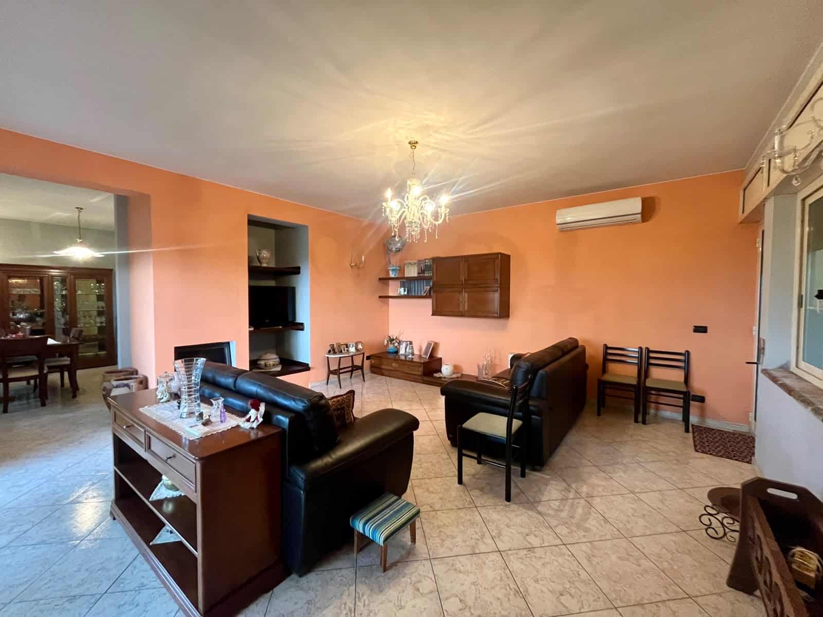 Interno soggiorno con pareti color pesca, divani in pelle nera, tavolino e lampadario elegante, aria condizionata e accessori decorativi, ambiente accogliente e luminoso.