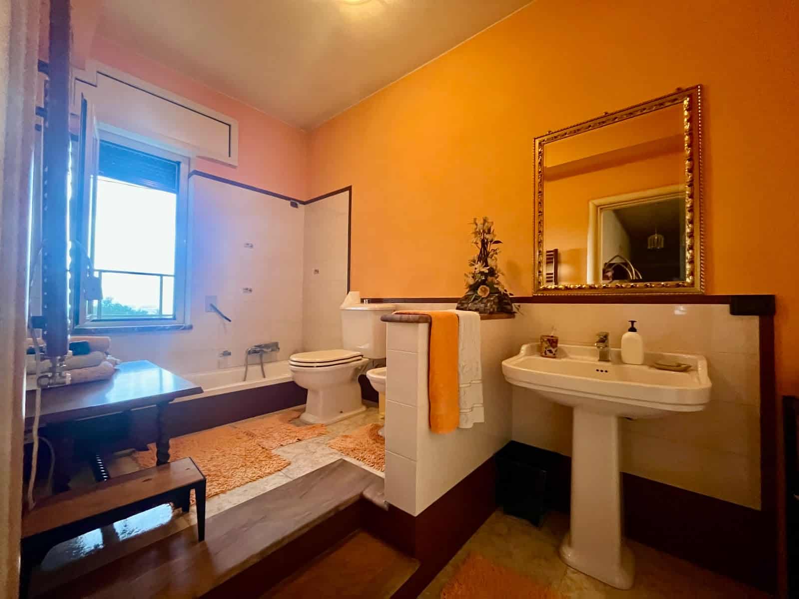 Il bagno spazioso con lavabo, specchio grande, WC e finestra luminosa, decorato con accessori eleganti e un tocco di verde, offre comfort e funzionalità in un ambiente accogliente e ben illuminato.