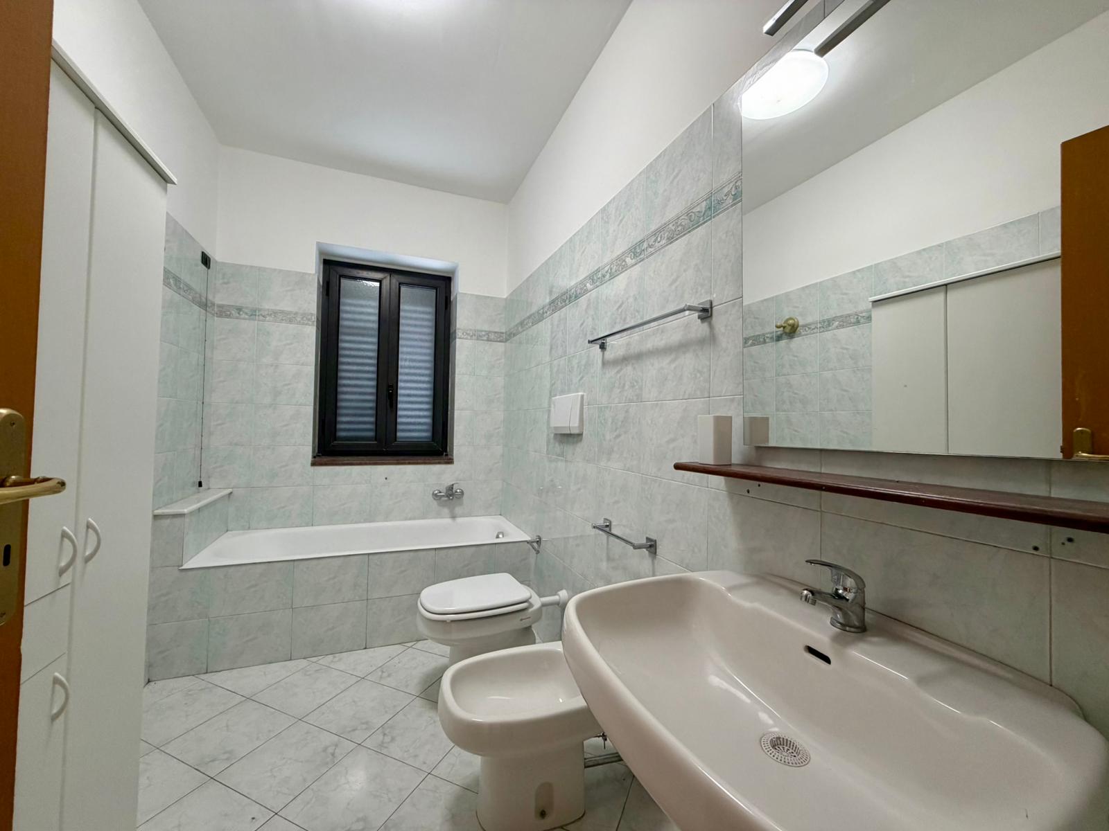 Lavabo e bagno con vasca, finestra e specchio grande, arredi moderni, ambiente luminoso e pulito, ideale per residenze e affitti turistici, rappresenta un esempio di bagno funzionale e ben progettato.