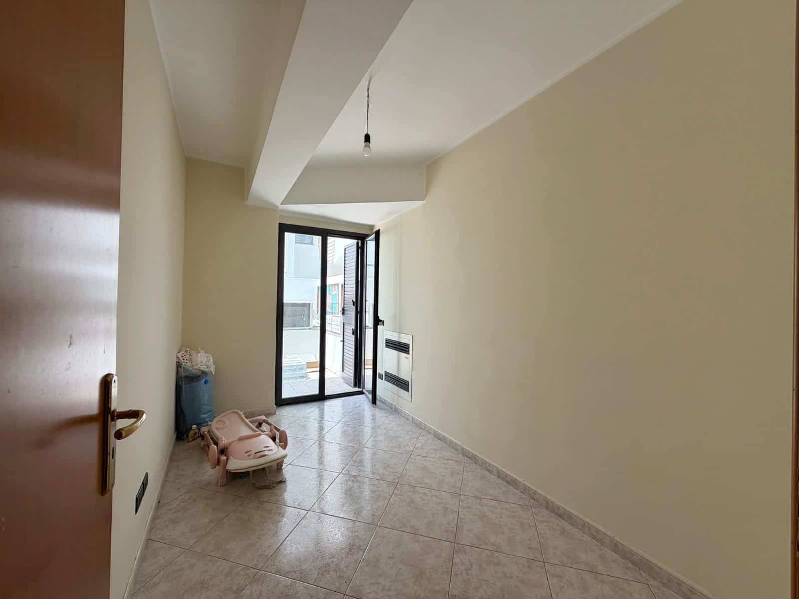 Stanza vuota in affitto con balcone e luce naturale, ideale per residenza o ufficio, con pavimento in piastrelle e pareti neutre.