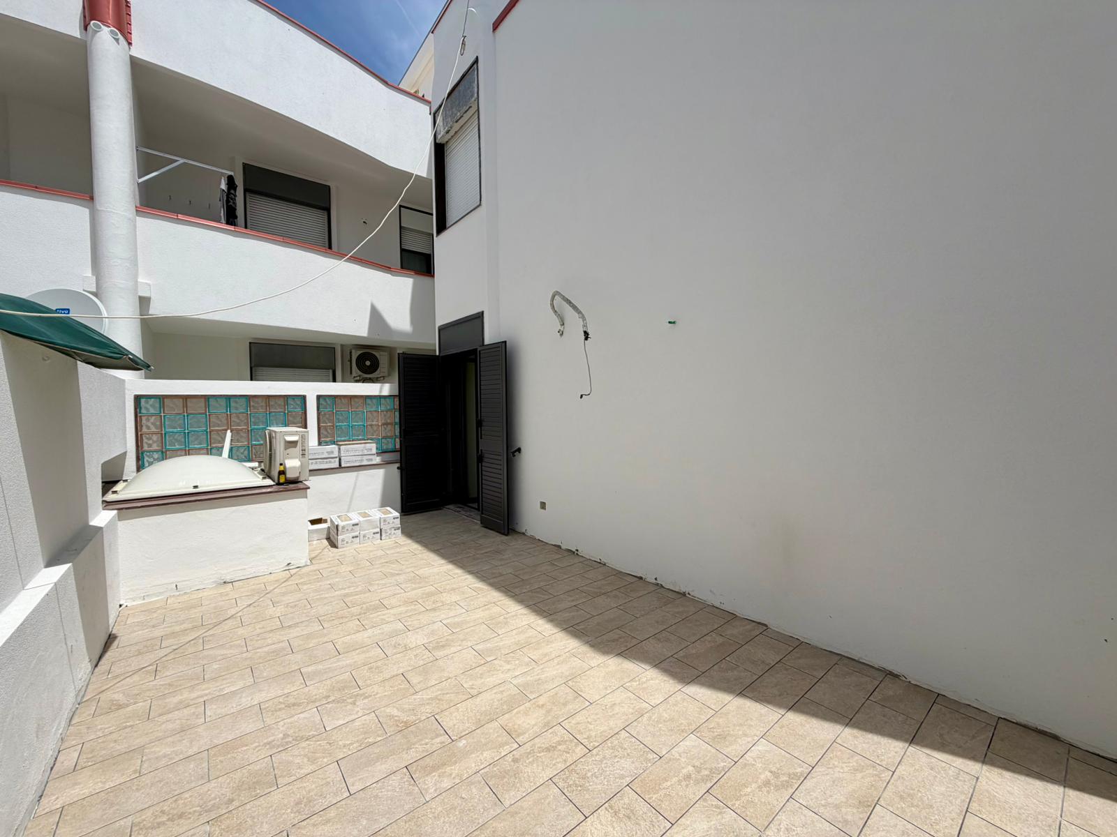 Ampia terrazza esterna con pavimentazione in piastrelle, ideale per relax e socializzazione, in un complesso residenziale moderno con balconi e spazi all'aperto.