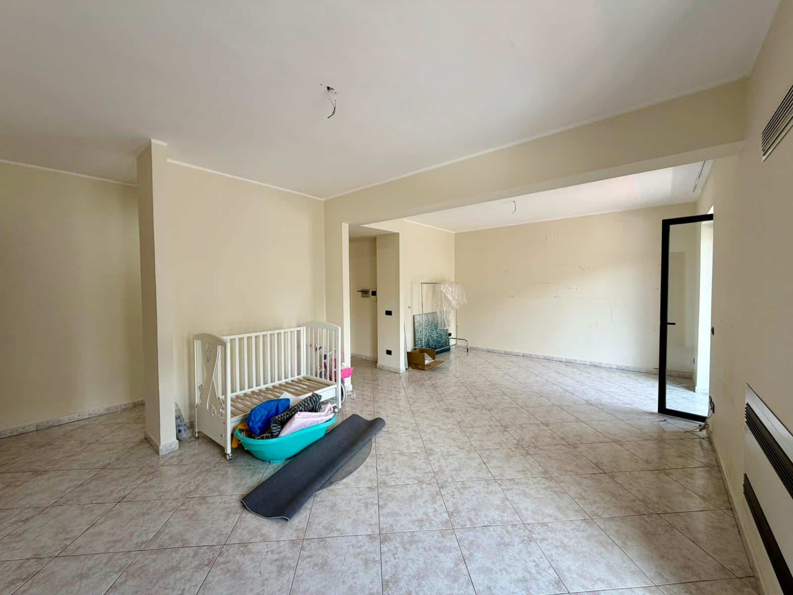 Aggiunta di un'area soggiorno vuota e luminosa con pareti neutre, pavimento in piastrelle e grandi finestre che permettono l'ingresso di luce naturale, ideale per la ristrutturazione o l'arredamento.