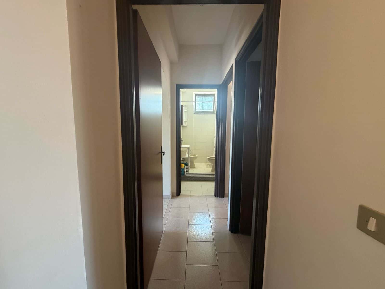 Interno di un appartamento con vista sulla stanza da bagno, pareti bianche e porte scure.