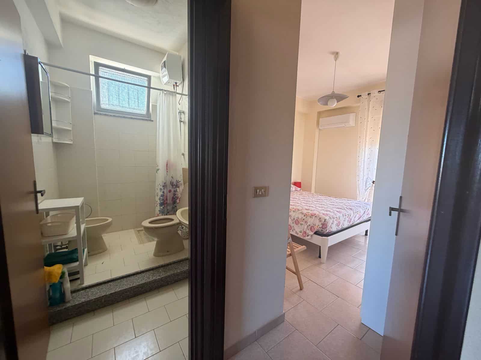 Interno di un appartamento con bagno e camera da letto, vista attraverso una porta aperta.